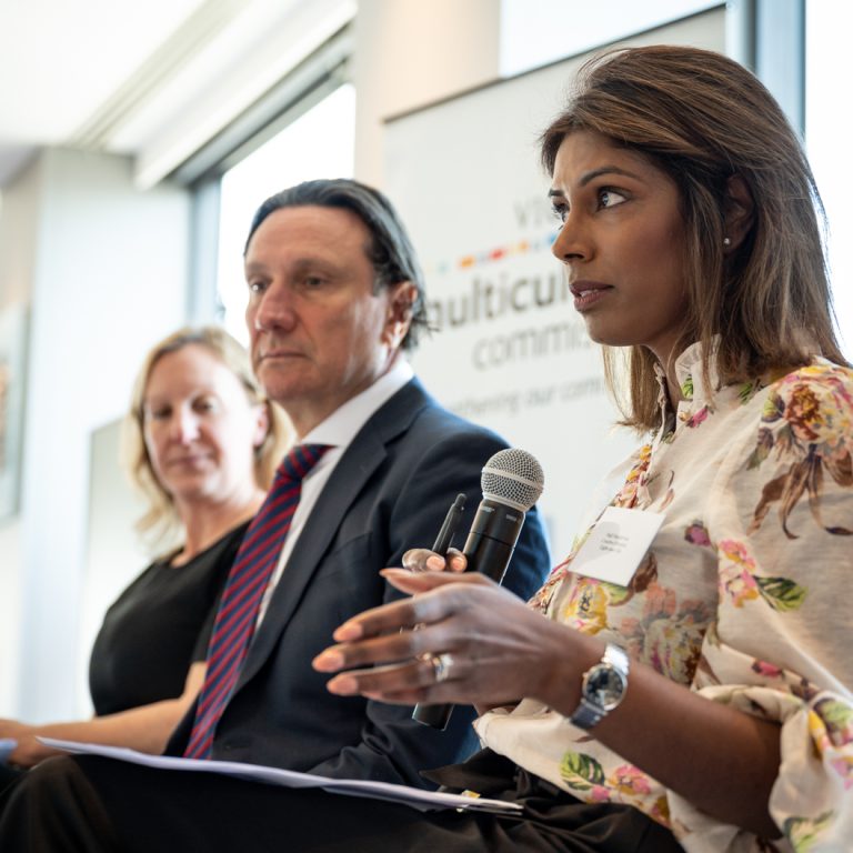 Businesswoman speaking during a multicultural leadership panel hosted by the Victorian Multicultural Commission, alongside fellow panelists in a bright, modern venue.