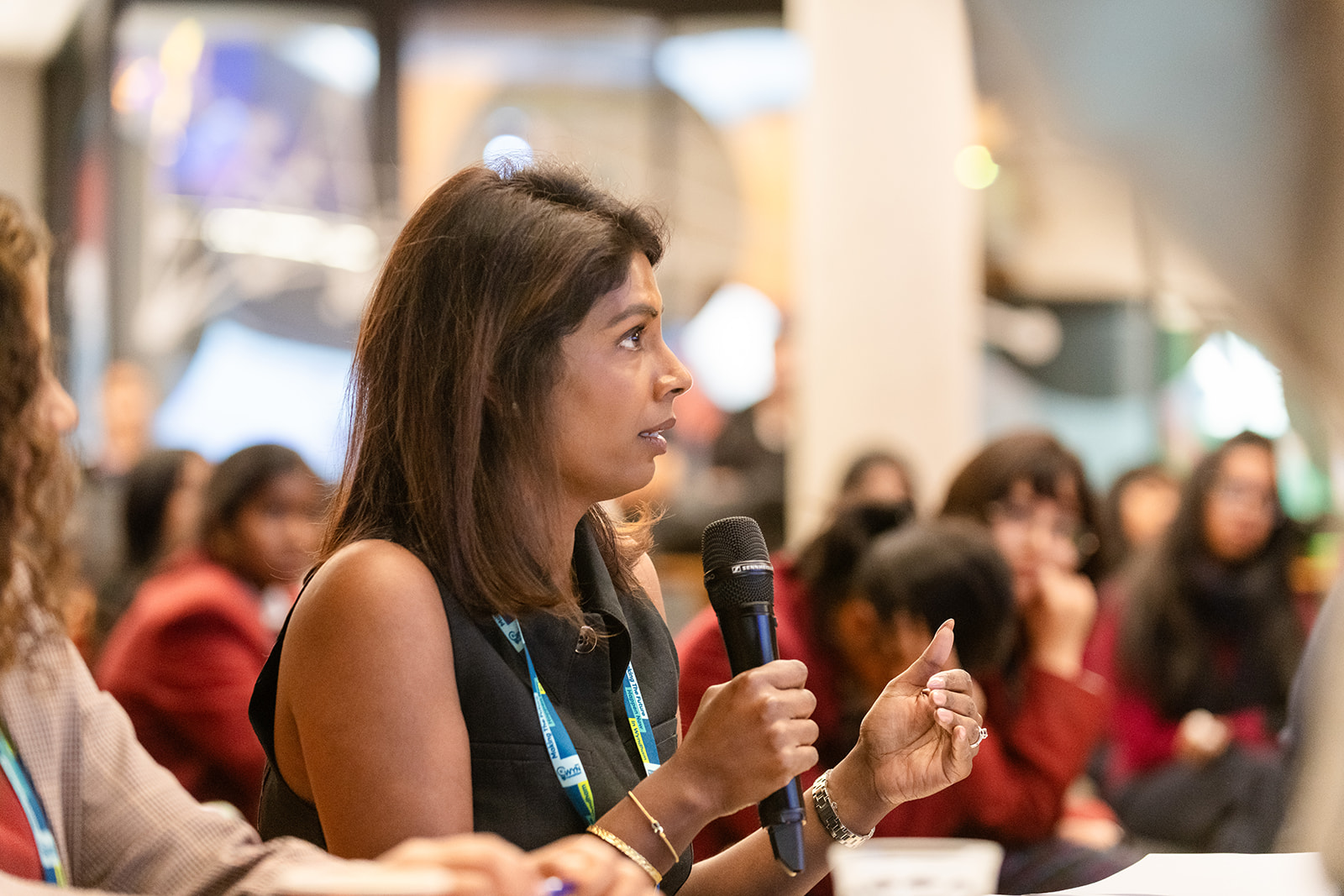 Woman speaking into a microphone at a professional conference panel, engaging attentively in front of a diverse seated audience